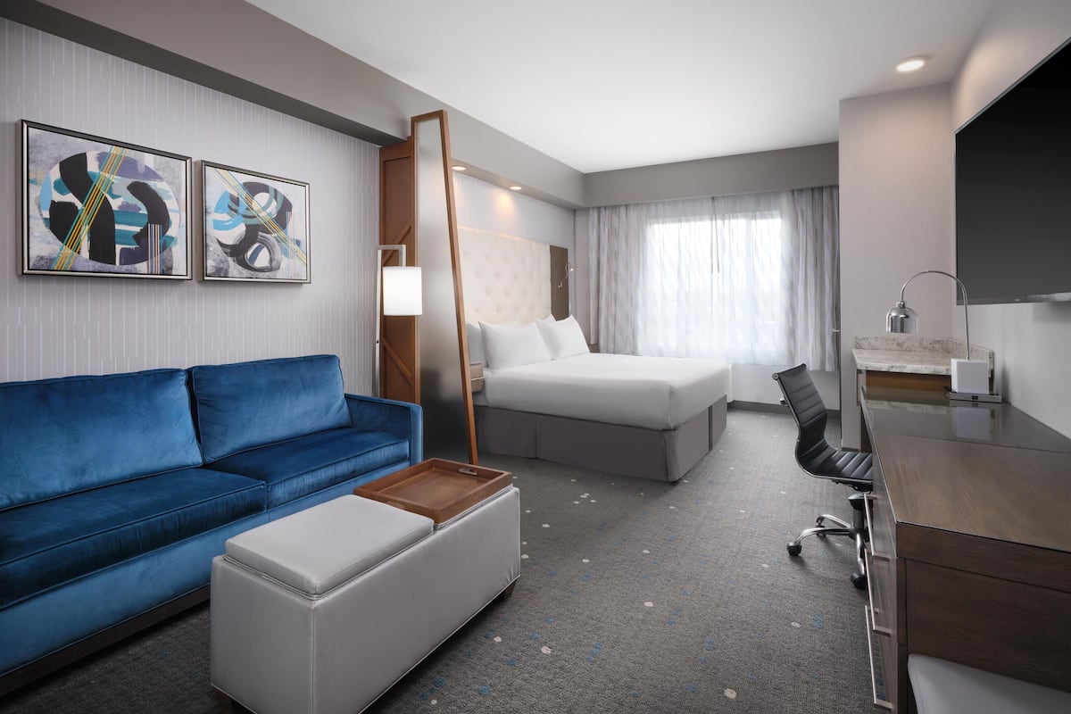 Una habitación de hotel con un sofá azul, una cama, un escritorio y un televisor.
