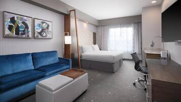 A hotel room with a blue sofa, a bed, a desk, and a TV.