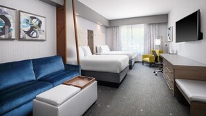A hotel room with a blue sofa, two beds, a desk, a chair, and artwork on the walls. - Best Western Premier Hotel at Fisher's Landing (Vancouver)