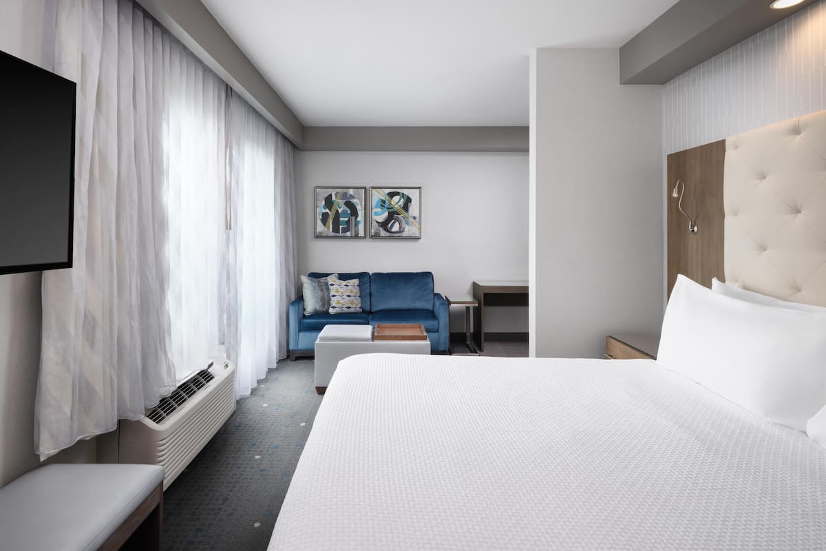 Una habitación de hotel moderna con una cama grande, un sofá, un televisor y una mesita.