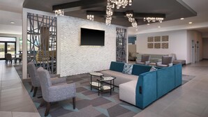 A modern living area with a sectional sofa, armchairs, a TV, and a decorative wall.