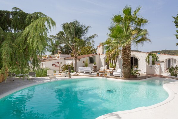 A pool area with a white pool, lounge chairs, and palm trees.