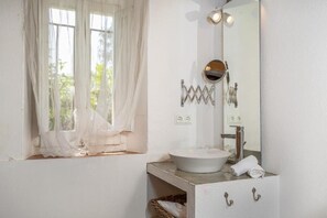 A bathroom with a white sink, a mirror, and a window with sheer curtains.