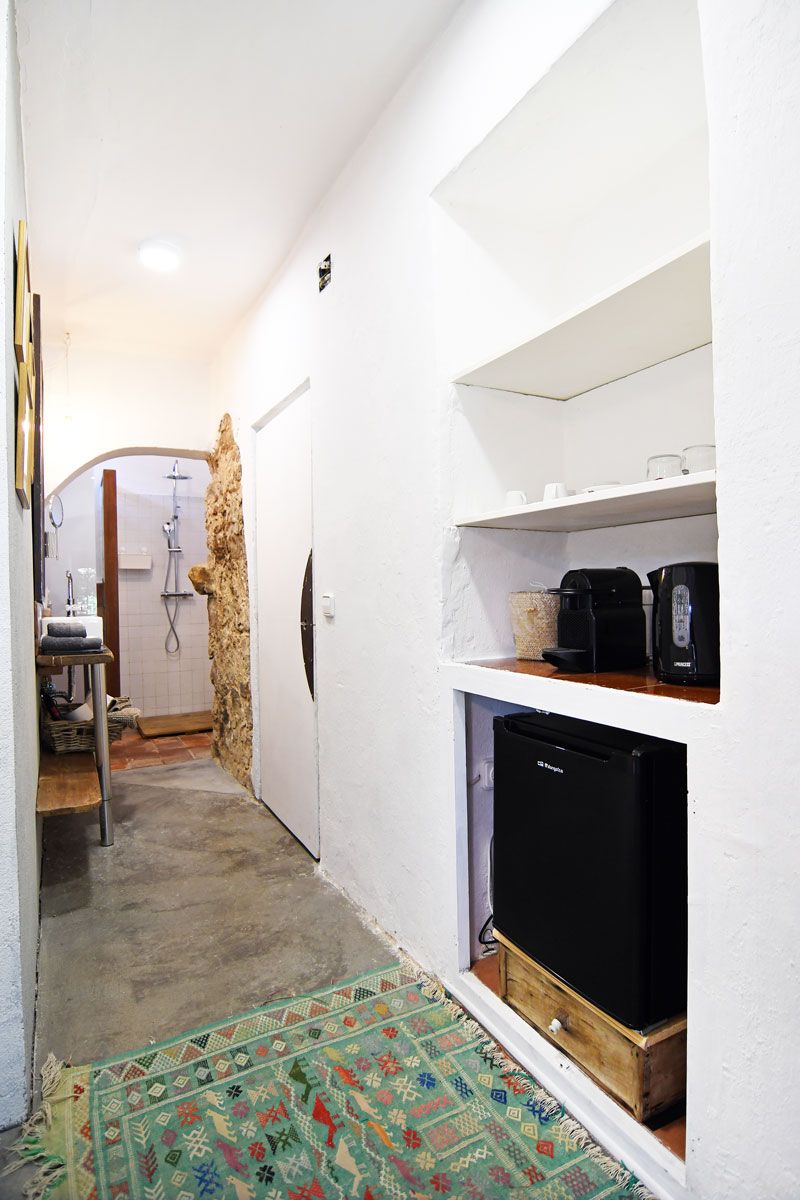 A narrow hallway with a shower area, a sink, and a shelf with a coffee maker and a black appliance.