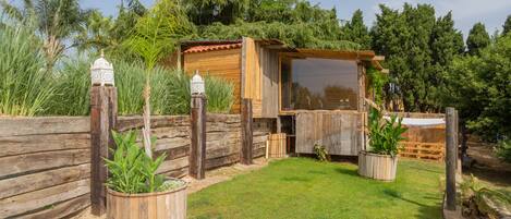 Una cabaña de madera con un porche cubierto, rodeada por una cerca de madera y macetas con plantas.