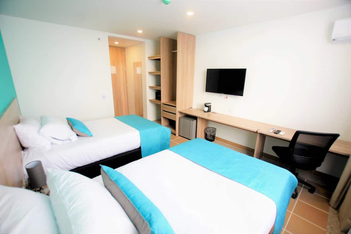 Une chambre d’hôtel avec deux lits, un bureau, une chaise, une télévision et une armoire.