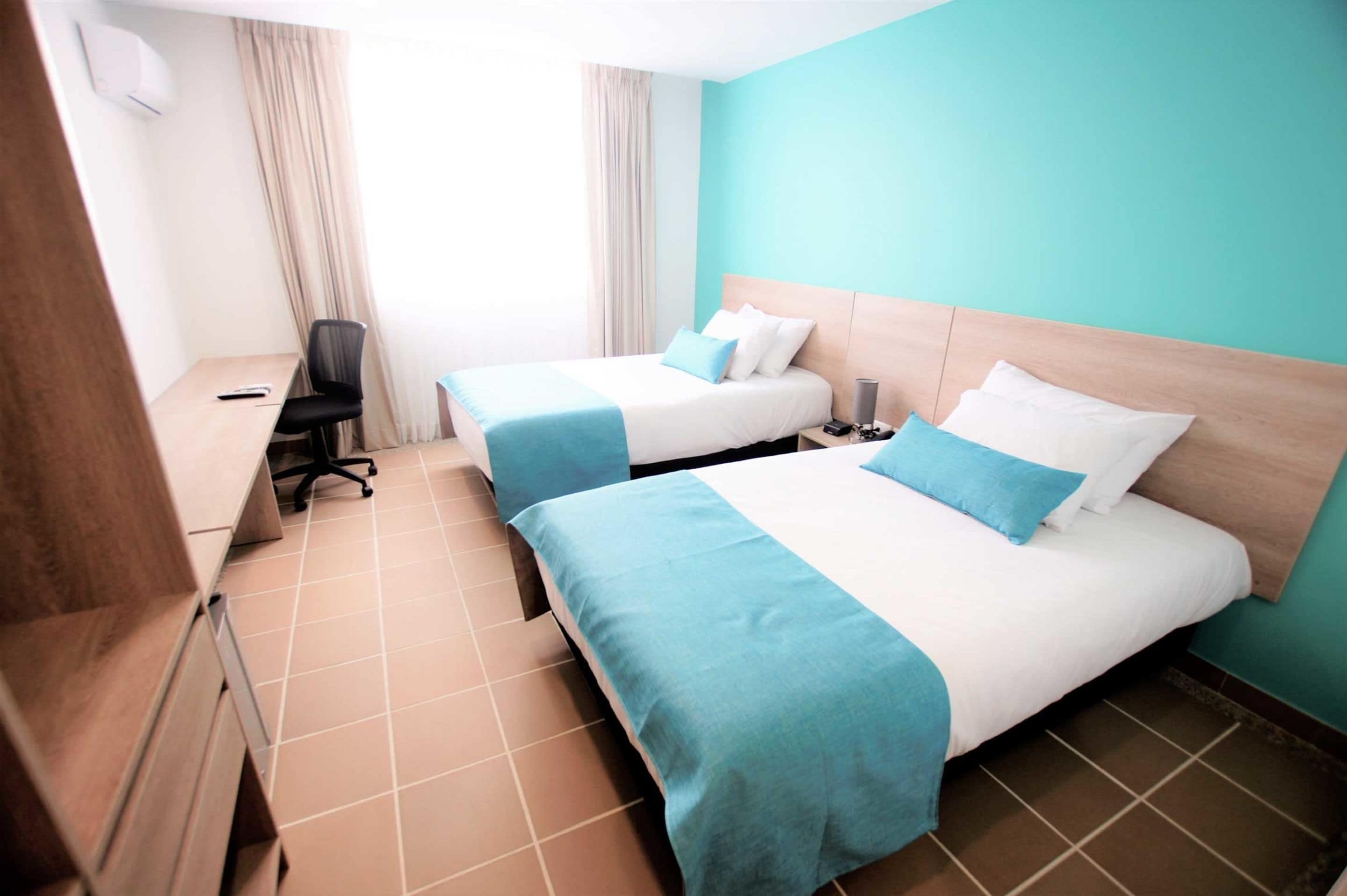 Ein Hotelzimmer mit zwei Betten, einem Schreibtisch, einem Stuhl und einem Fenster mit Vorhängen.
