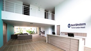 A hotel lobby with a reception desk, a seating area, and a view of the outside.