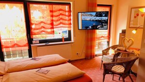 A hotel room with two beds, a television, a wicker chair, and a heart-shaped decoration on the wall.