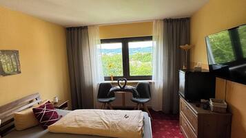 A hotel room with two beds, a desk with a chair, a television, and a window with a view of greenery.