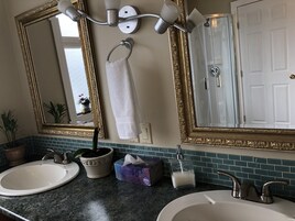 A bathroom with two sinks, a mirror with a gold frame, a towel hanging on the wall, and a door.