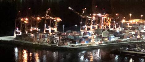 A nighttime view of a port with cranes and containers, reflecting on the water.