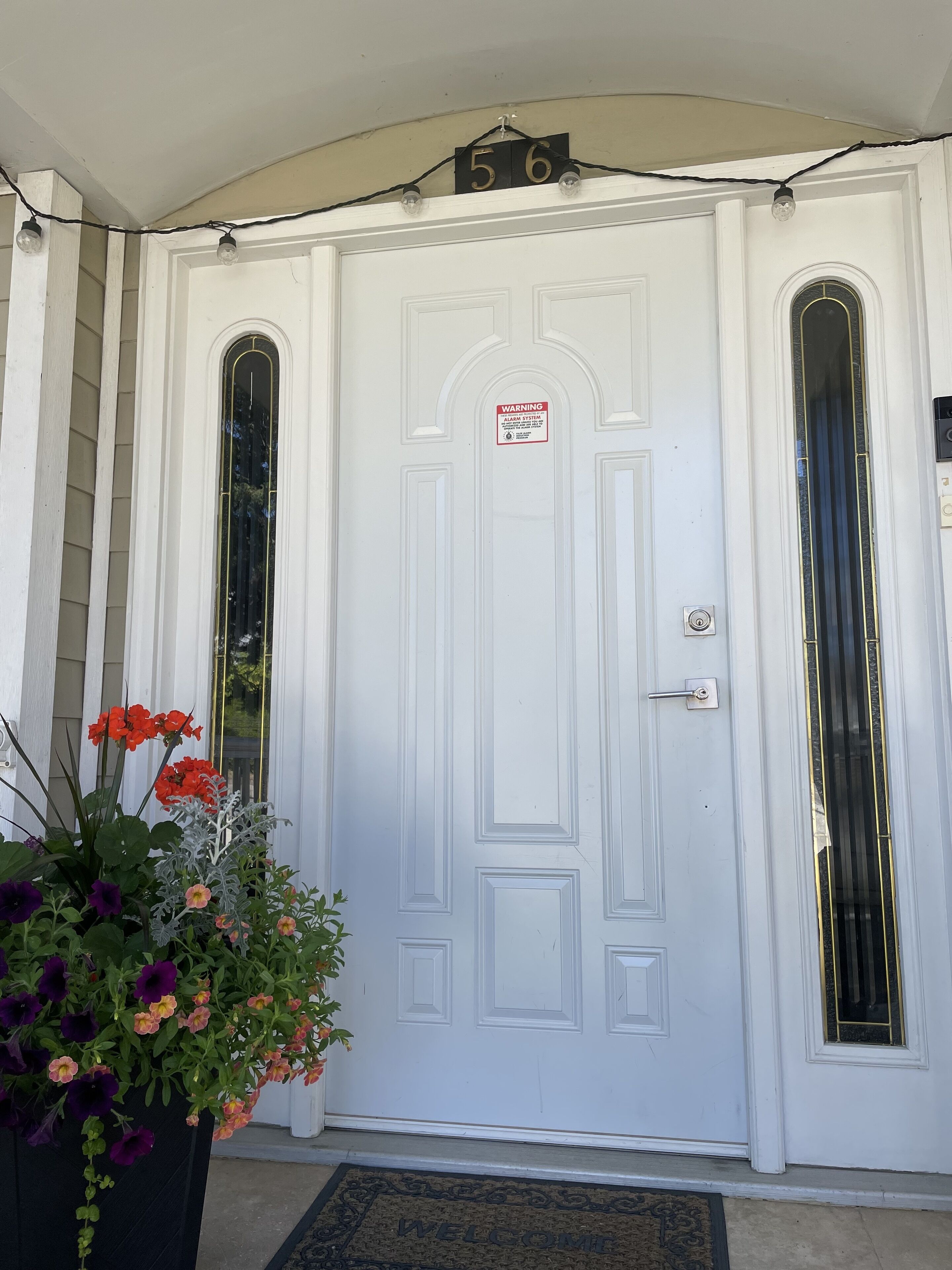 A white front door with a warning sign, a number plaque, and a welcome mat.