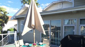 Une table de jardin ronde, avec des chaises, un parasol et un barbecue.