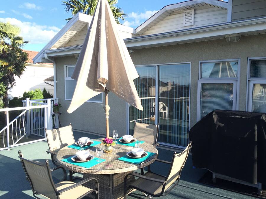 A round outdoor dining table with chairs, a table umbrella, and a grill.