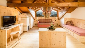 A cozy wooden interior with a TV, sofa, and dining area, featuring a mountain view through a large window. - Family & Wellness Hotel Shandranj (Tesero)