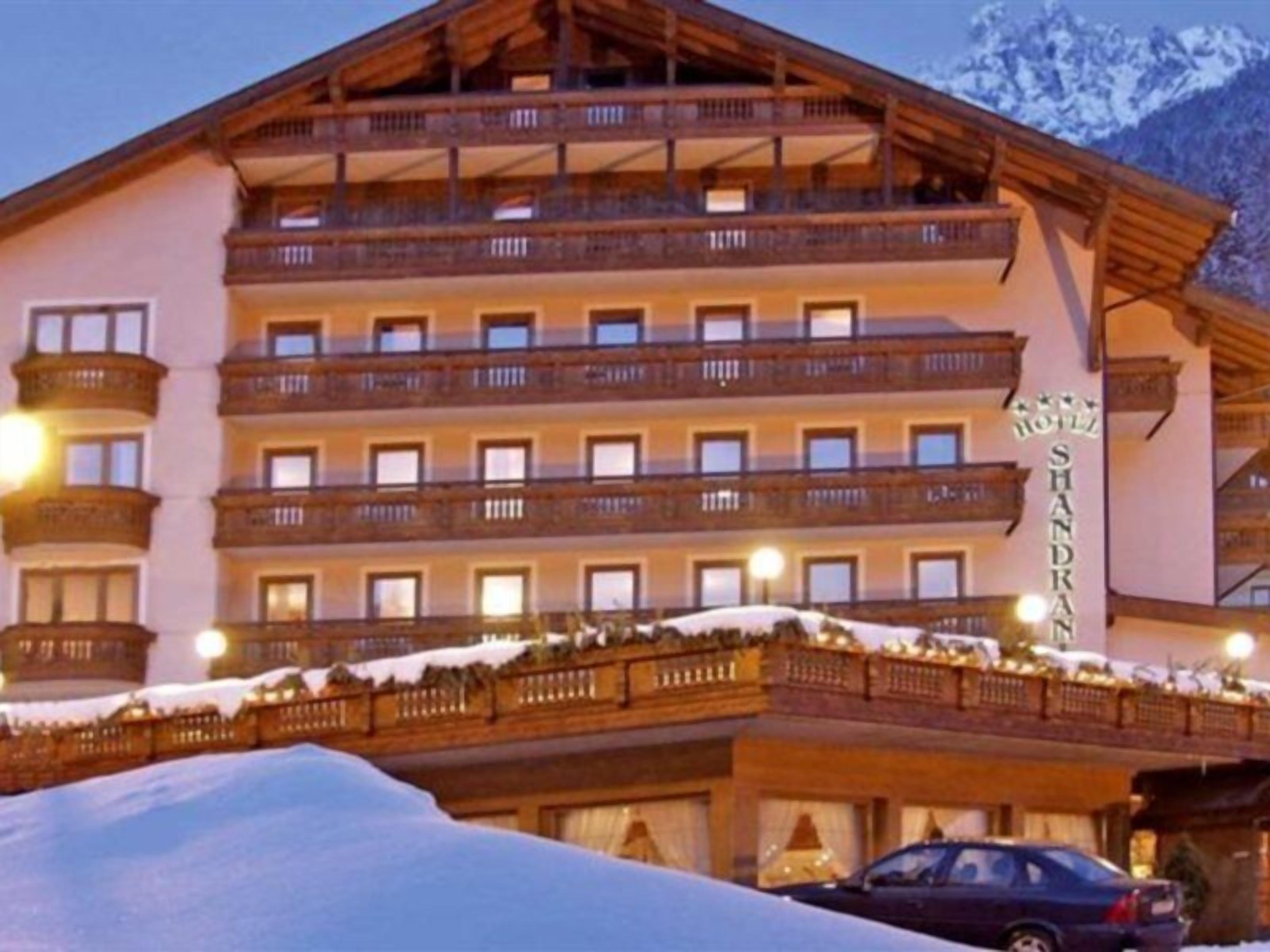Ein mehrstöckiges Hotel mit Balkonen, einem Schild mit der Aufschrift 'Hotel Shandran' und Schnee auf dem Dach.