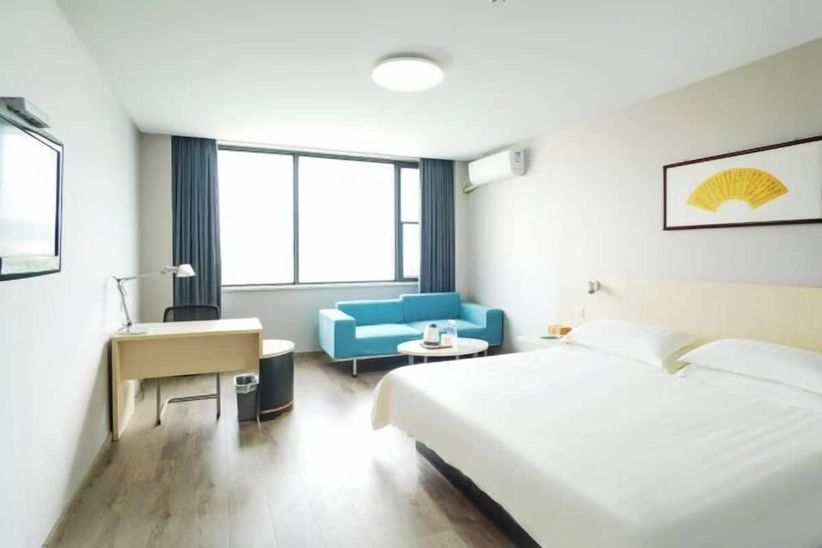 Habitación de hotel con cama, escritorio, silla, mesita, sofá y ventana grande.