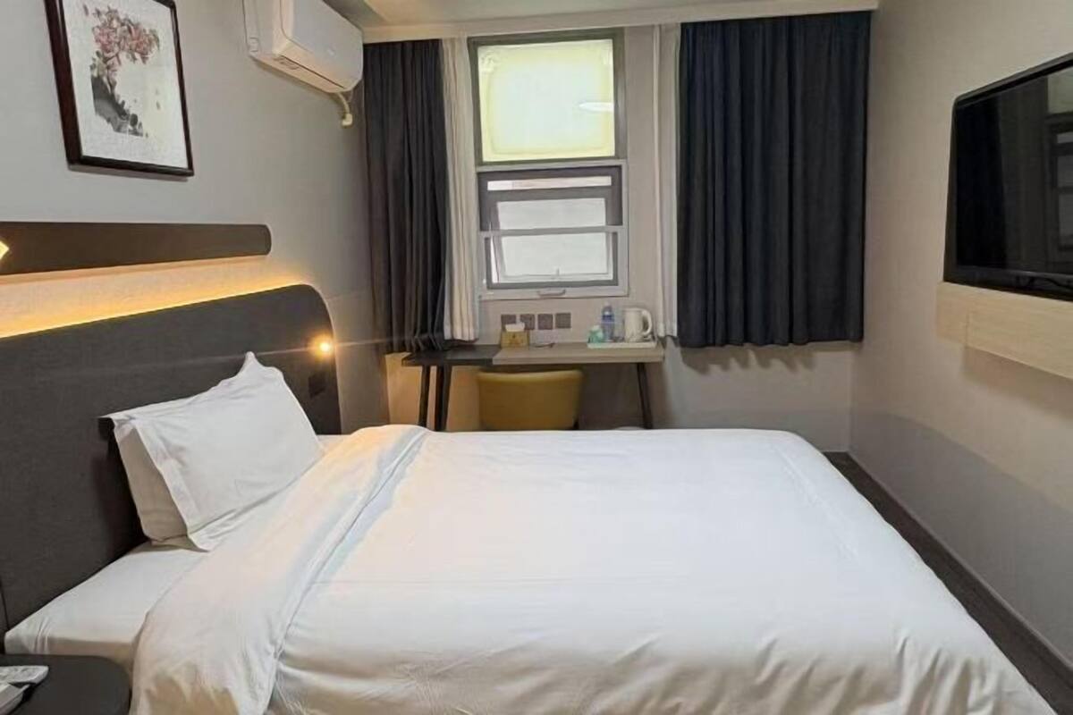 Habitación de hotel con cama, escritorio, silla, televisión y ventana con cortinas.