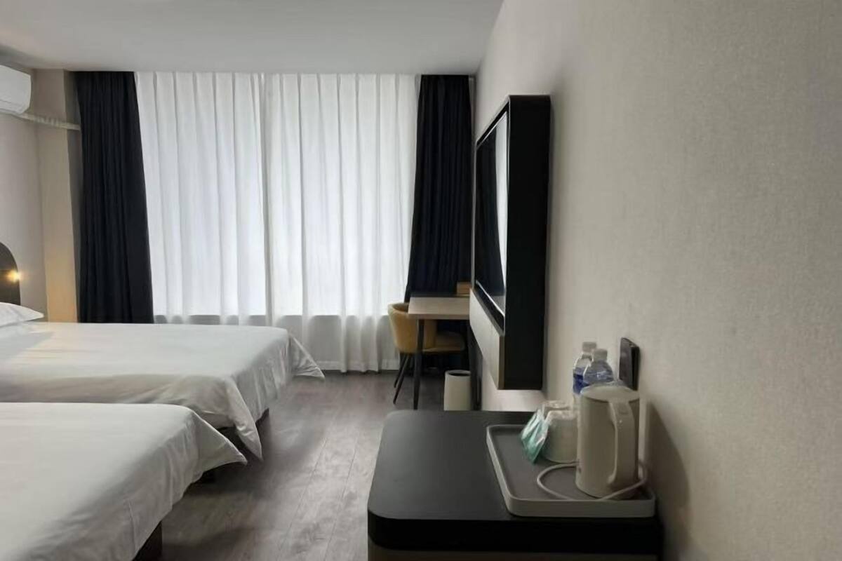 Habitación de hotel con dos camas, un escritorio, una silla, un televisor de pantalla plana y una mesita con una tetera y botellas de agua.