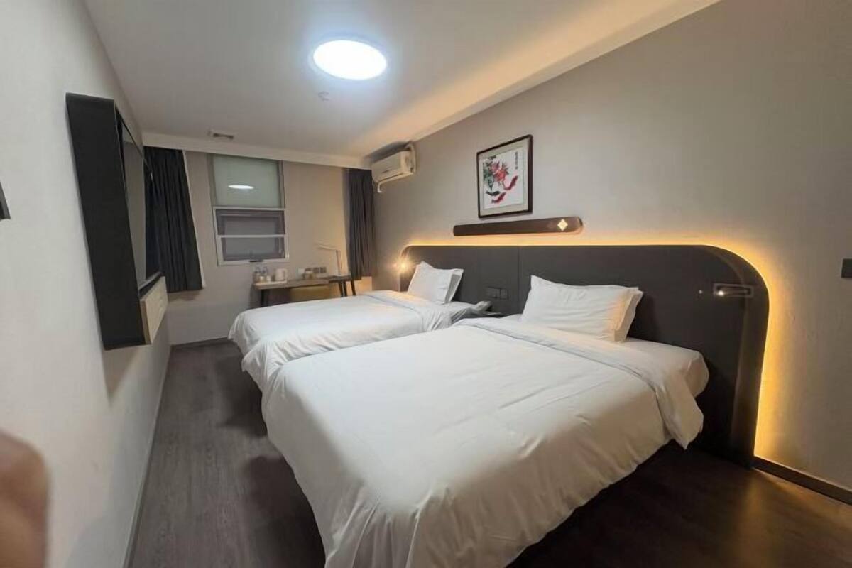 Una habitación de hotel con dos camas, una kitchenette pequeña, una ventana y una lámpara en el techo.