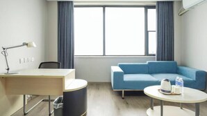Ein modernes Hotelzimmer mit Schreibtisch, einem blauen Sofa, einem runden Tisch und einem großen Fenster mit Vorhängen.
