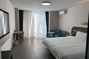 Egy modern szállodai szoba, amelyben egy nagy ágy, egy íróasztal székkkel, egy kis, kerek asztal és egy kanapé található.