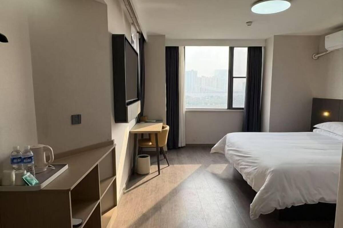 Una habitación de hotel con cama, escritorio, silla, televisor y ventana con vista a la ciudad.