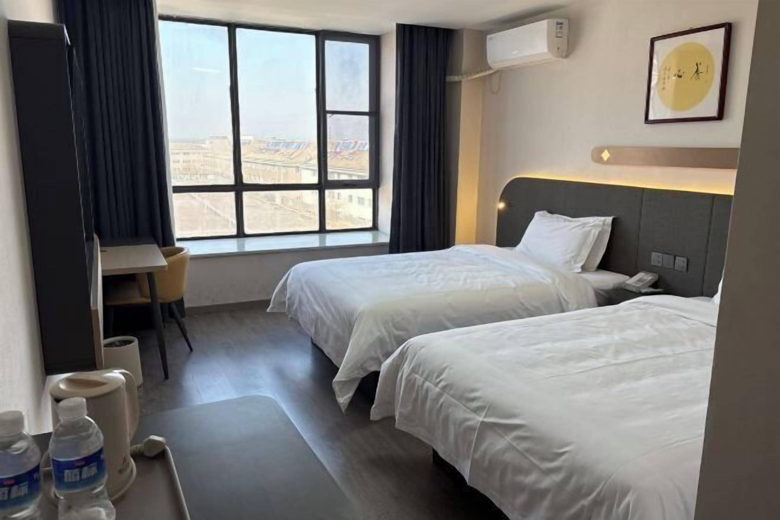 A hotel room with two beds, a desk, and a window offering a city view.