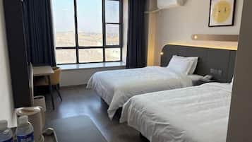 Habitación de hotel con dos camas, un escritorio y ventana con vista a la ciudad.