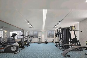 Een sportschool met trainingsapparatuur, grote ramen en een blauwe, patroonrijke vloer.