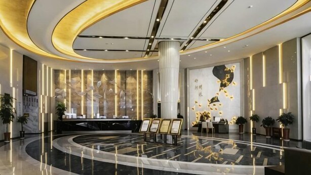 Un moderno vestíbulo de hotel con un mostrador de recepción circular, una columna grande y una pared decorativa.