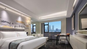 Una habitación de hotel moderna con una cama grande, un área de comedor y vistas a la ciudad.
