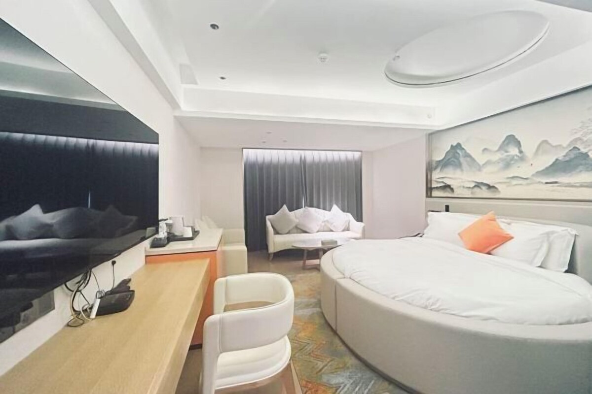 Ein modernes Hotelzimmer mit einem großen Bett, einem Schreibtisch mit Stuhl, einem Flachbildfernseher und einem Bild an der Wand.