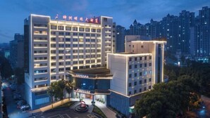 Un hotel de varios pisos con fachada moderna, señalización iluminada y una zona de estacionamiento al frente.