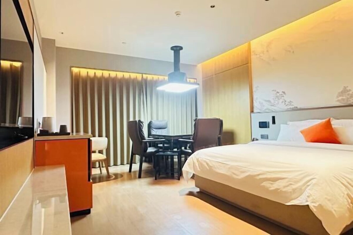 Ein Hotelzimmer mit Bett, Schreibtisch, Stuhl, Tisch und einem großen Fenster mit Vorhängen.