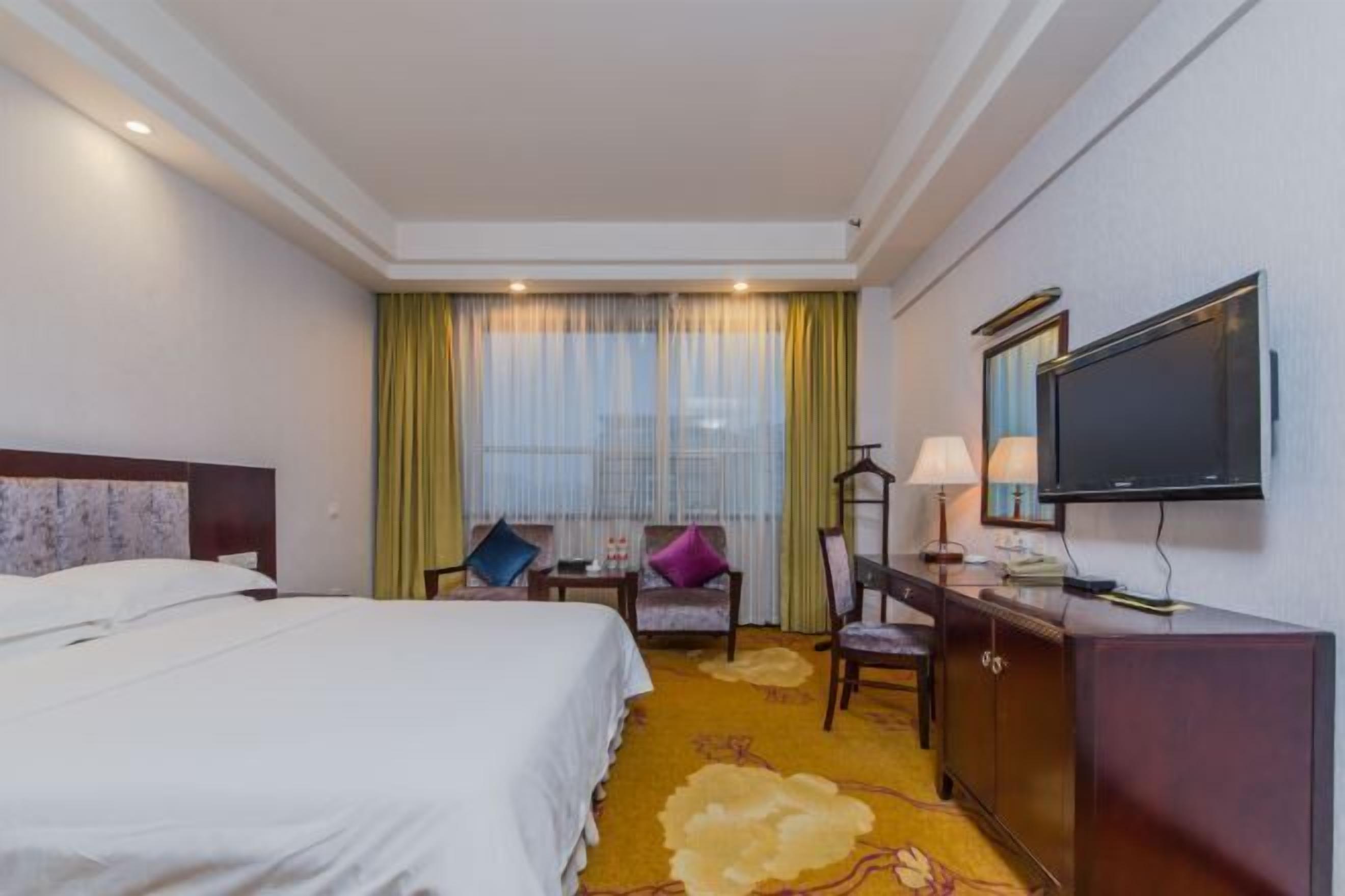 A hotel room with a bed, a desk, a chair, a television, and a window with curtains.