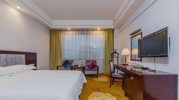 A hotel room with a bed, a desk, a chair, a television, and a window with curtains.