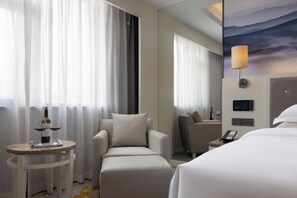 Ein Hotelzimmer mit Bett, zwei Sesseln, einem kleinen Tisch mit einer Weinflasche und einer Wandlampe.