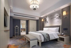 Ein modernes Hotelzimmer mit einem großen Bett, Nachttisch, Bank, Kleiderschrank und einem Fernseher.