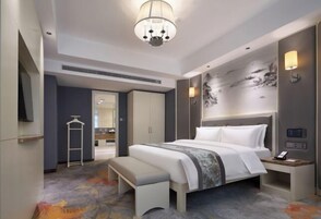 A modern hotel room with a large bed, bedside table, bench, wardrobe, and a television.