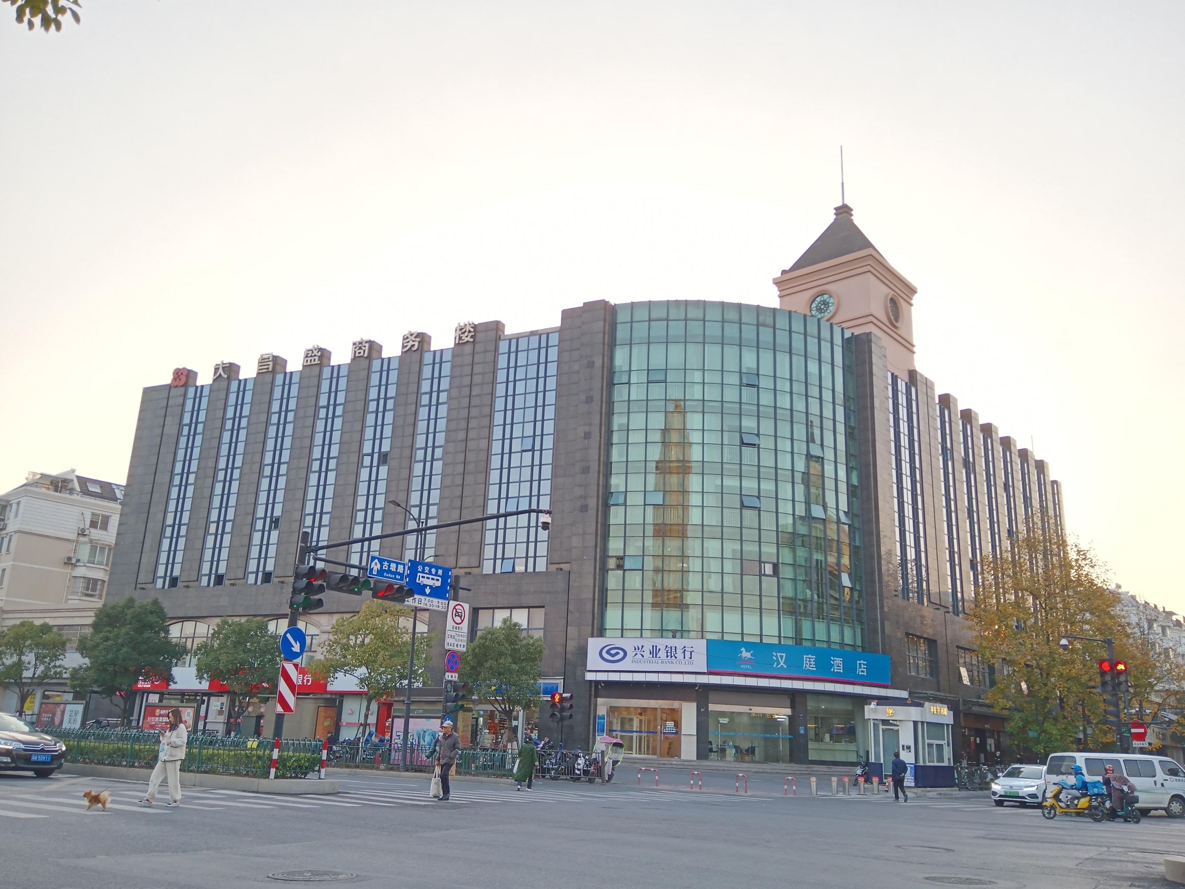 A modern building with a curved glass facade, a clock tower, and signage for an industrial bank and a hotel.
