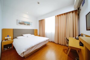 A hotel room with a bed, bedside tables, a desk, a chair, a painting, and a window with curtains.