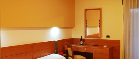 Habitación de hotel con cama, escritorio, silla, espejo y ventana con cortinas.
