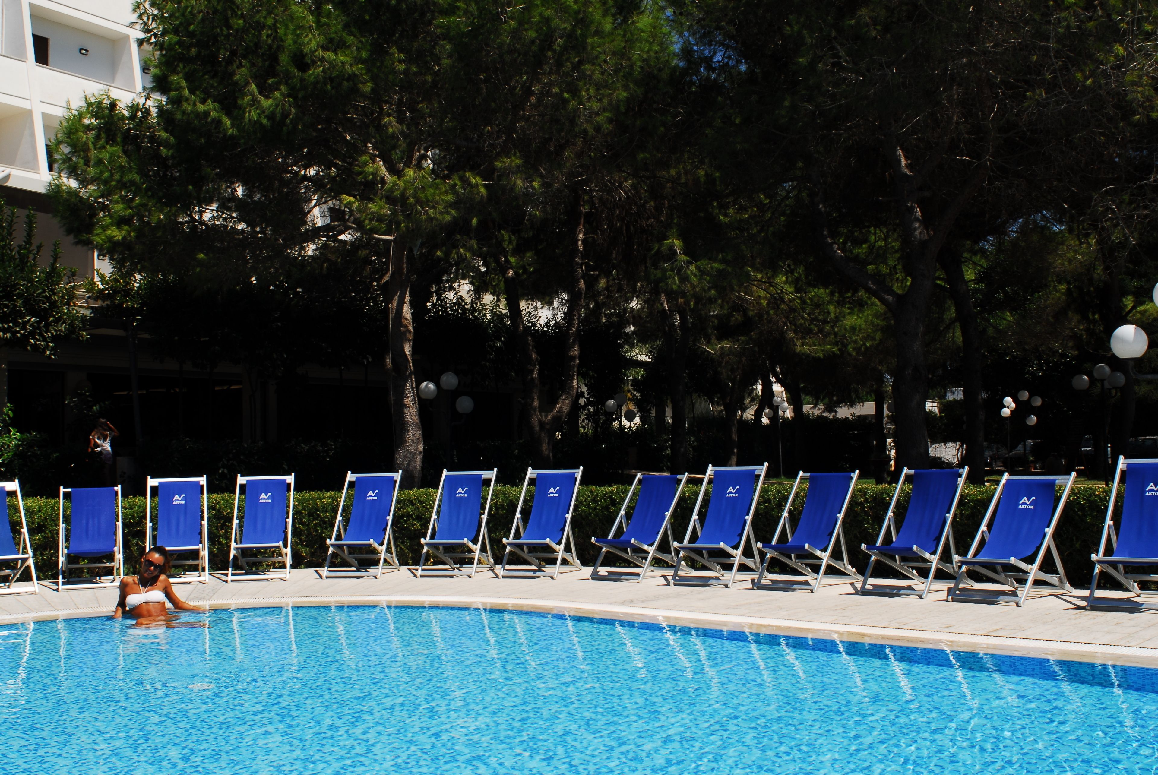 A swimming pool with blue water, surrounded by blue lounge chairs and trees.