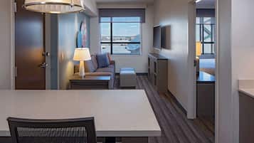 Una habitación de hotel compacta con una mesa de comedor, un sofá, un televisor y una ventana con vistas a la ciudad.