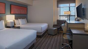 A hotel room with two beds, a desk, a chair, a TV, and a window with a view.