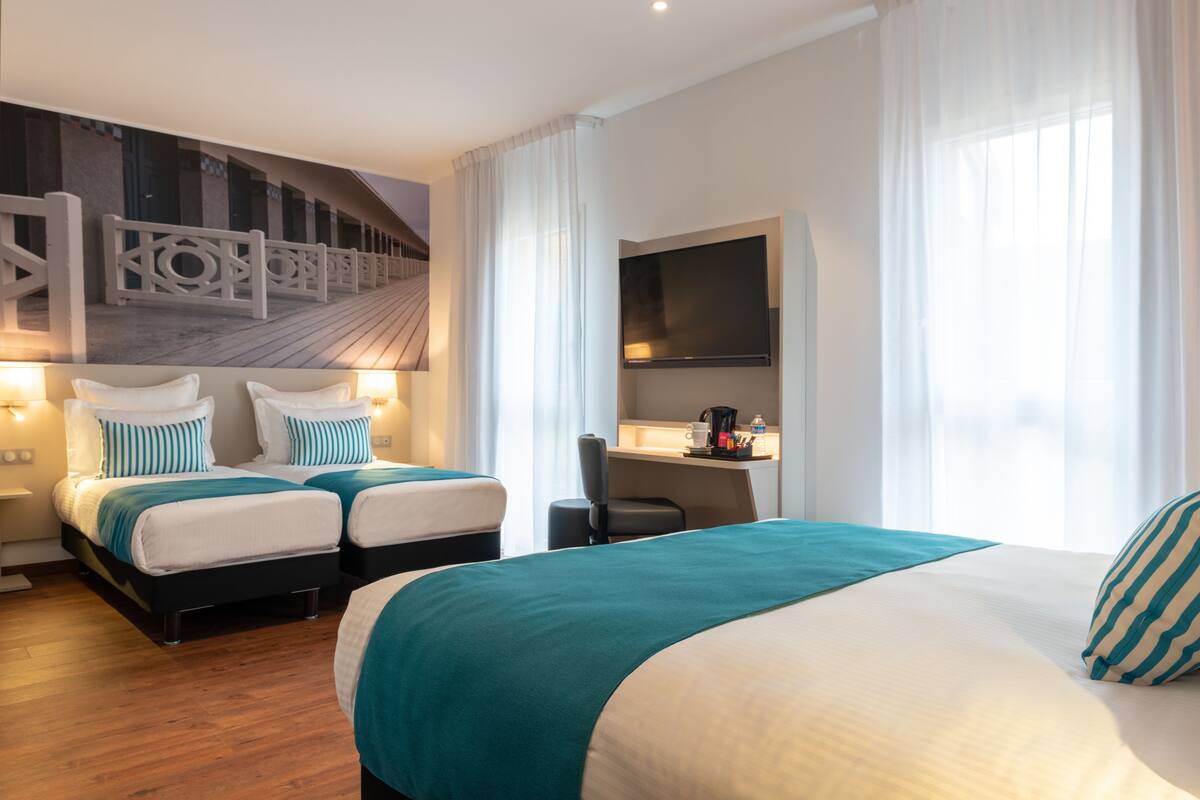 Une chambre d’hôtel avec deux lits, un bureau doté d’un téléviseur à écran plat et une grande fenêtre avec des rideaux.
