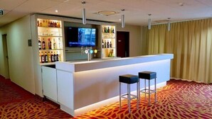Vestíbulo de hotel con zona de bar que incluye un televisor de pantalla plana, estantes con licores y dos taburetes.