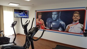 Un gimnasio con equipo de ejercicio, un televisor mostrando un evento deportivo y un cartel grande de un boxeador.